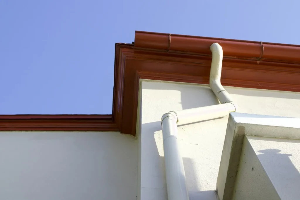 A clean gutter and downspout attached to the side of a building after flushing