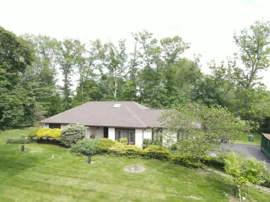 A suburban house under mature tree cover, the shade conditions that grow roof algae