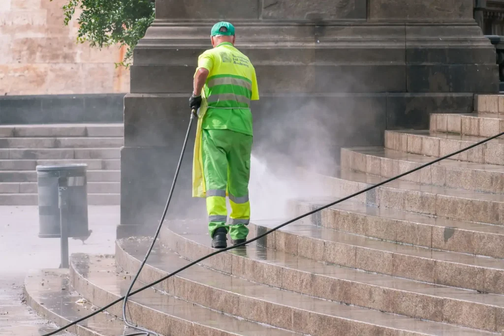 Municipal worker power washing stone steps