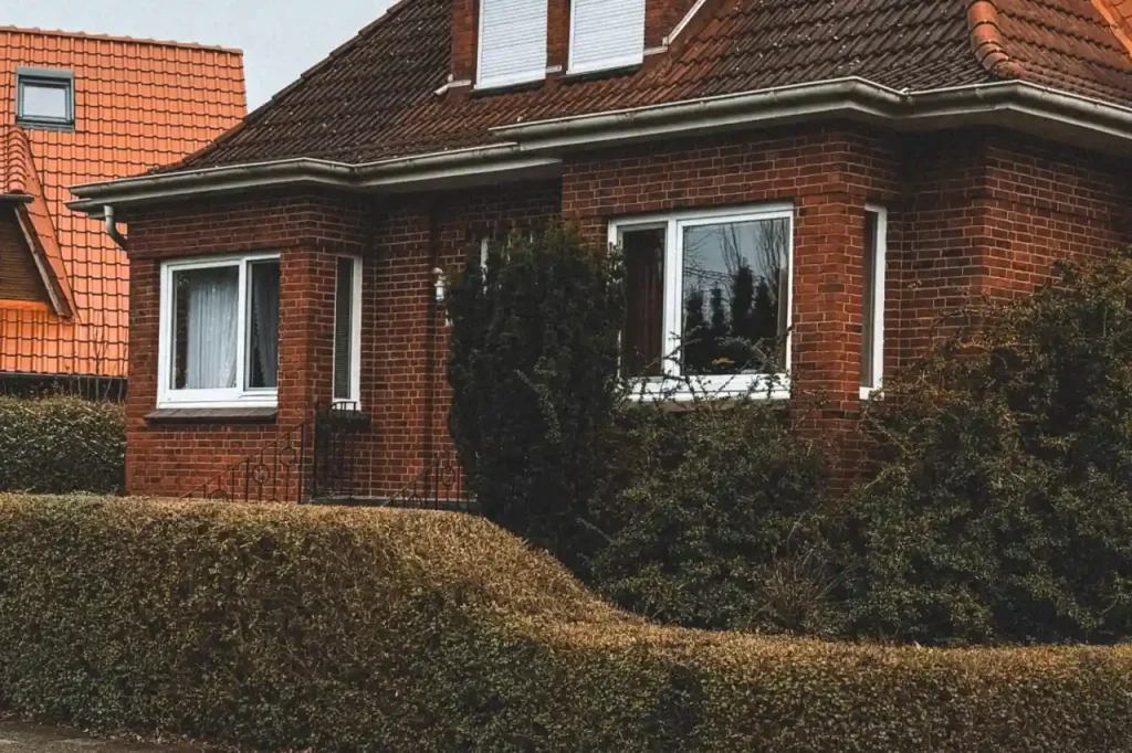 Red brick house with a sloped roof and hedges