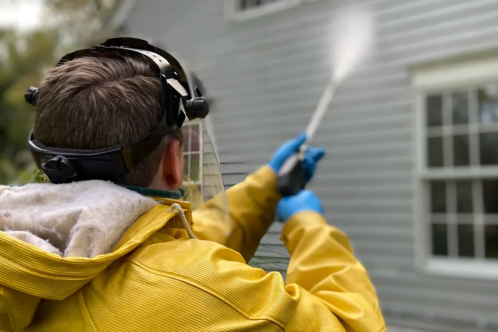 Technician pressure washing house siding in protective gear