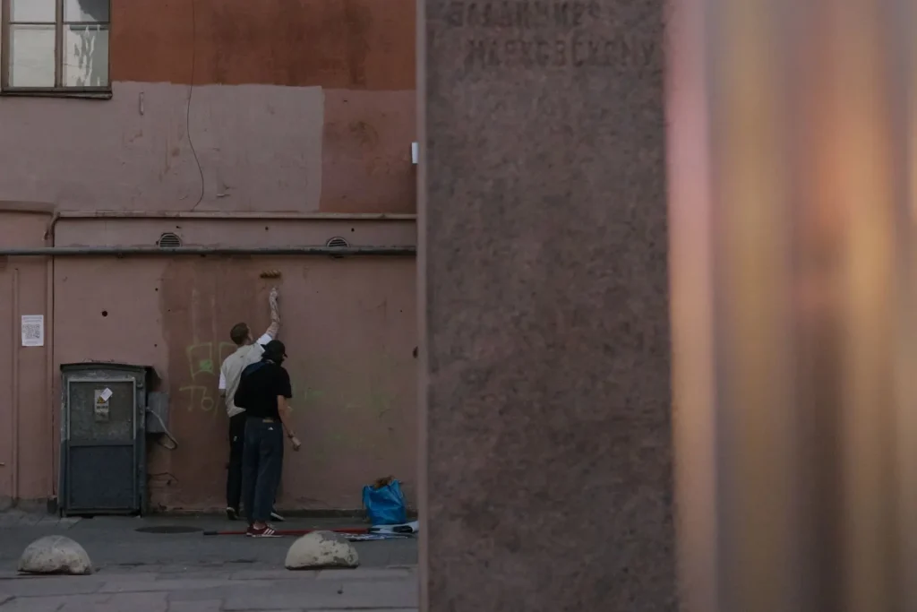 Two workers painting over a city wall