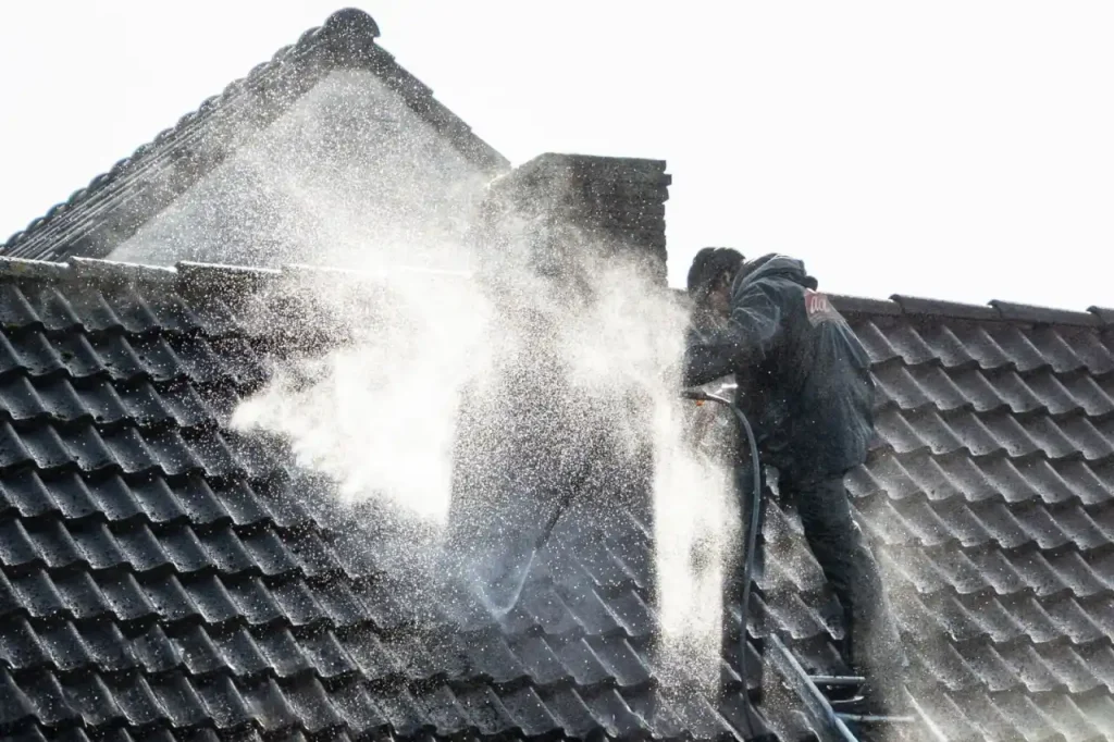 Worker power washing roof tiles to remove grime and buildup