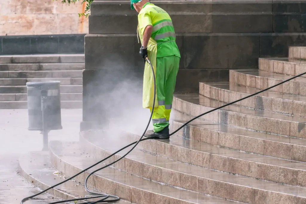 Worker pressure washing stone steps in a public park